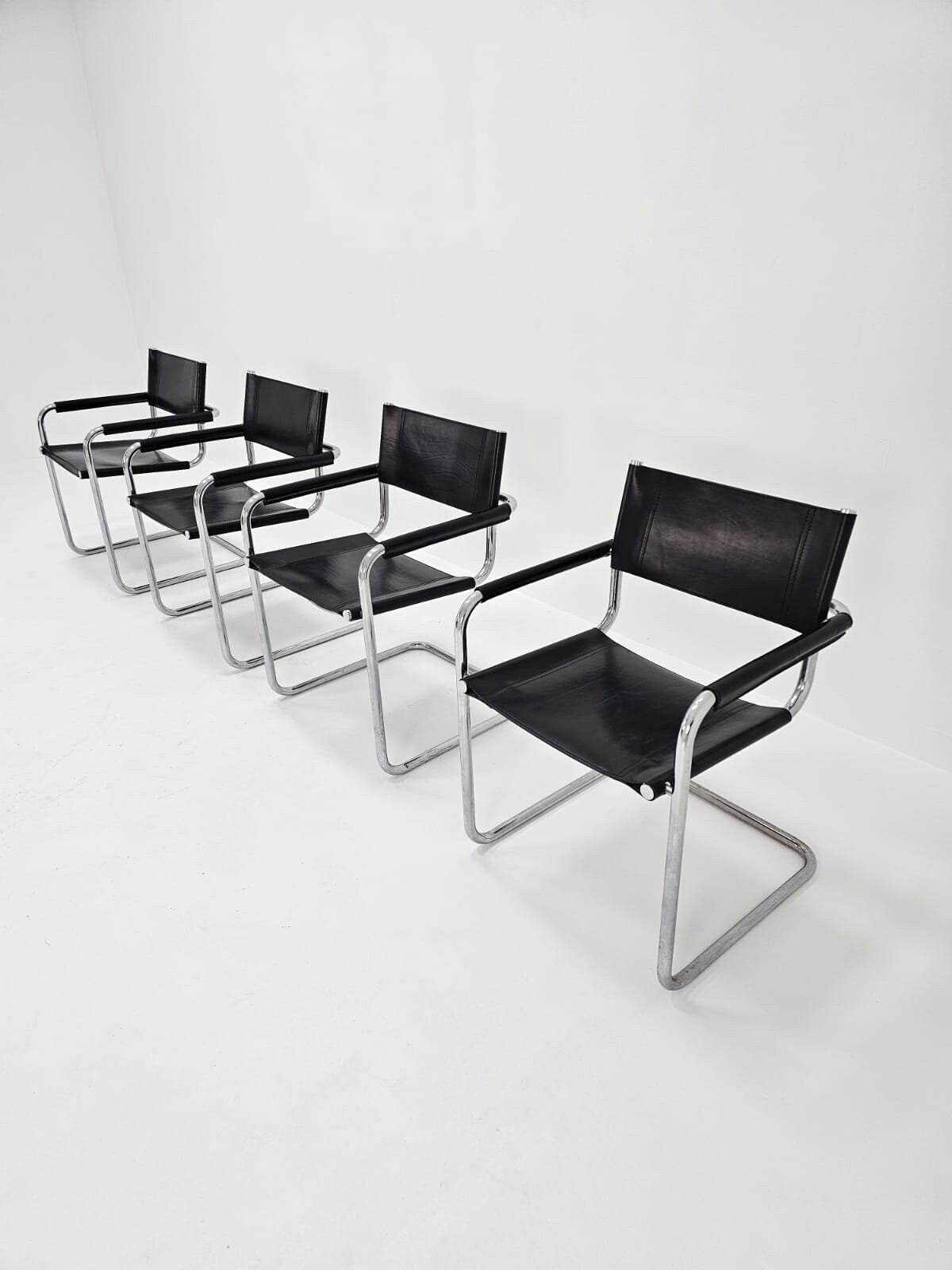 May include: Four black leather and chrome chairs arranged in a row. The chairs have a simple, modern design.